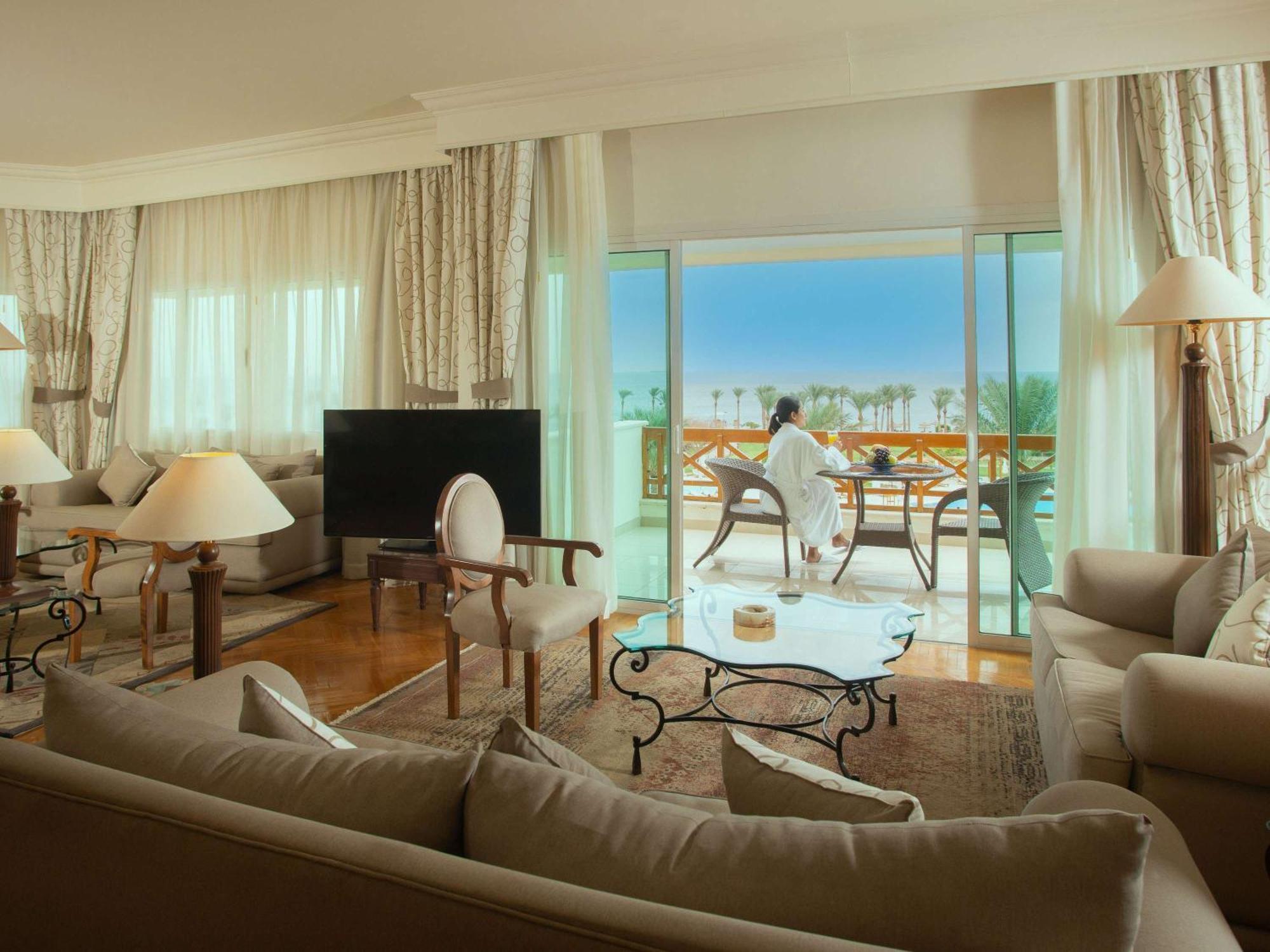 모벤픽 리조트 타바 외부 사진 The photo depicts a luxurious hotel suite. Inside, there is a spacious living area with elegant furnishings, including a large sofa, stylish armchairs, and a glass coffee table. A flat-screen TV is positioned in one corner. The large windows allow na